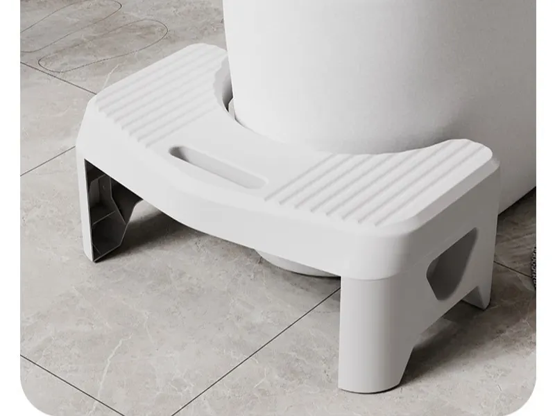 A white plastic footstool tucked against the base of a toilet