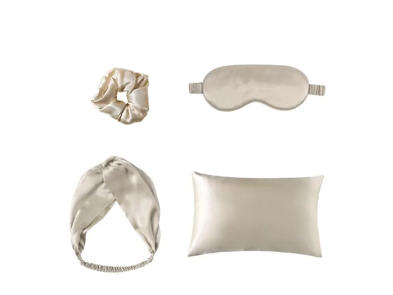 A champagne-coloured satin eye mask, pillowcase, scrunchie and twisted headband laid out on white
